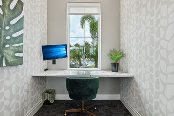 A white desk with a green chair and a blue monitor in front of a window. at The Junction at Rockledge Apartments, Florida